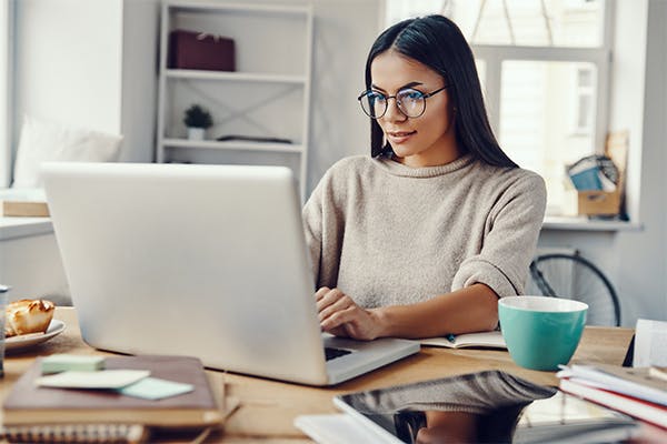 Beautiful-young-woman-in-casual-clothing-using-laptop-and-smiling-while-working-indoors