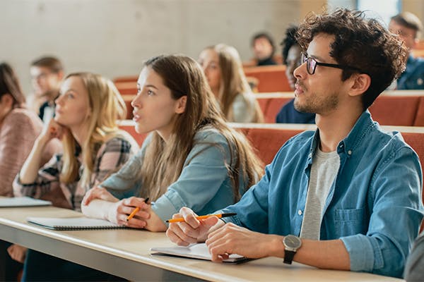 In-the-Classroom-Multi-Ethnic-Students-Listening-to-a-Lecturer-and-Writing-in-Notebooks.